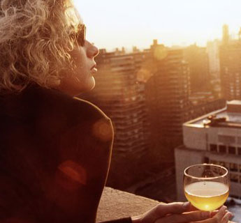 Woman with sunglasses watches sunset on balcony with glass of wine